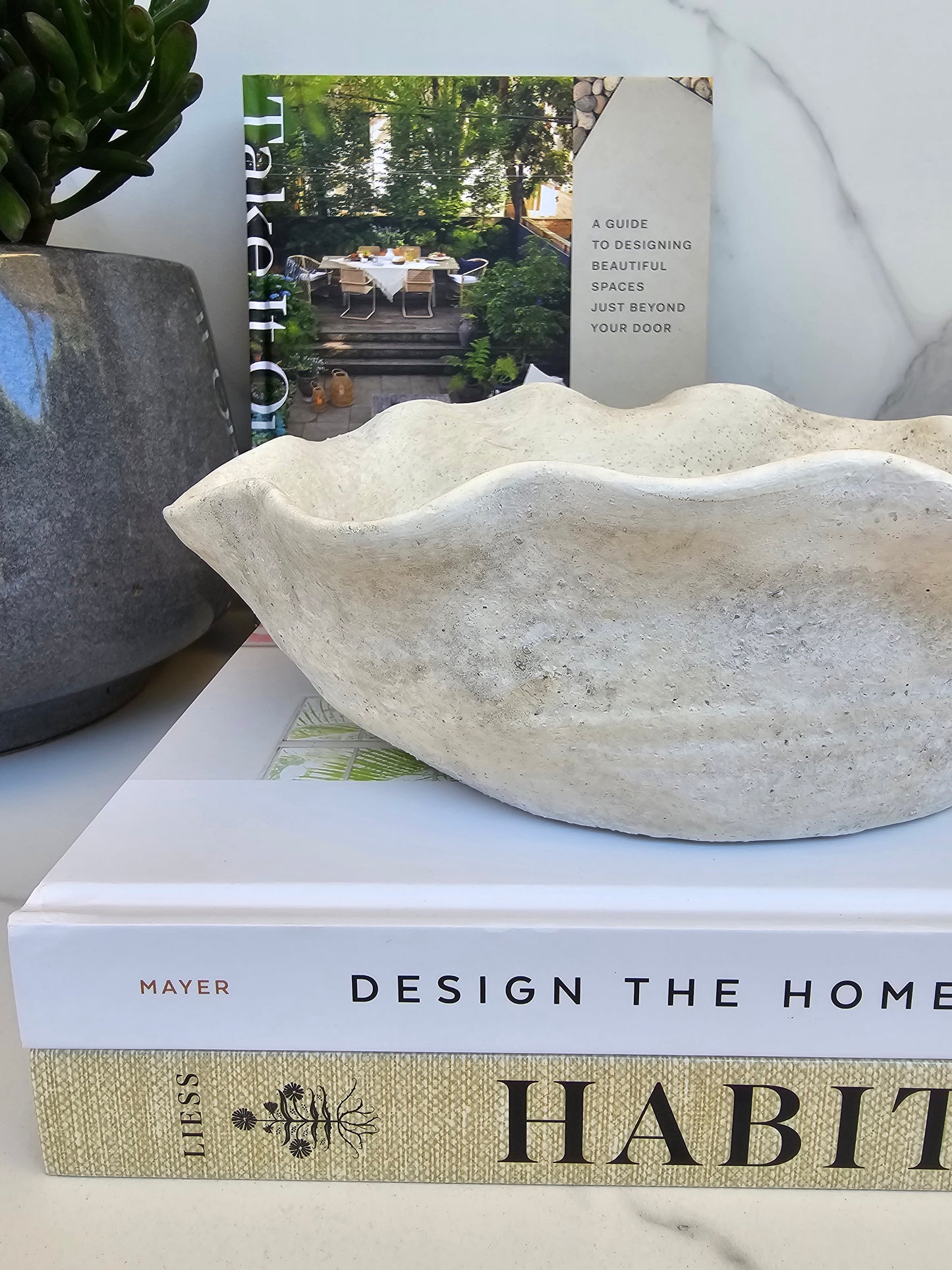 Organic stone bowl planter with sculptural wavy edges styled on coffee table books in a neutral modern interior