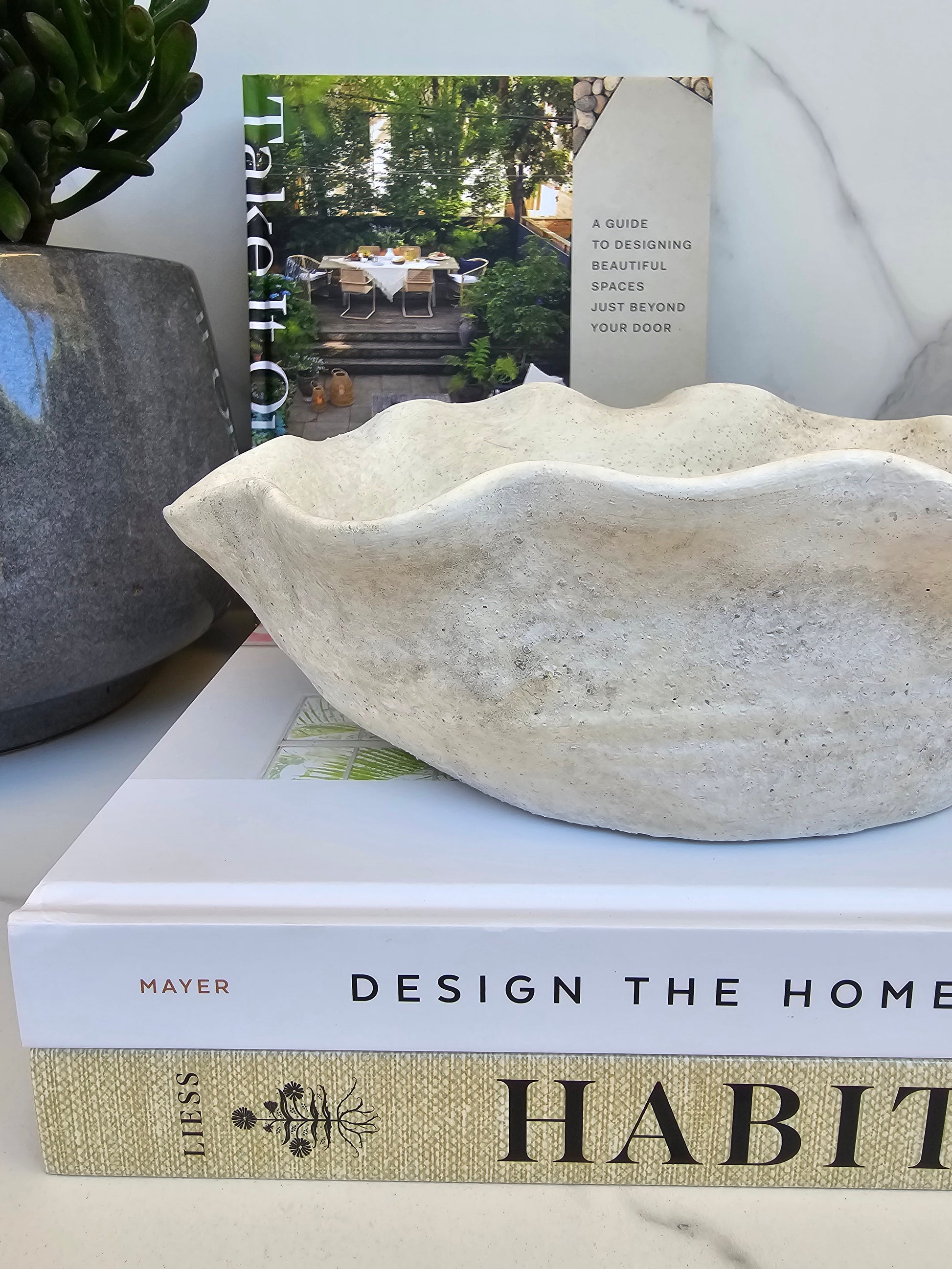 Organic stone bowl planter with sculptural wavy edges styled on coffee table books in a neutral modern interior